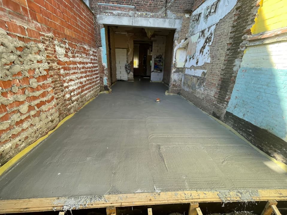 Gladgestreken betonplaat tussen de bestaande muren, klaar voor de volgende laag